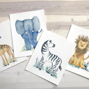 Pu&ograve; includere: Quattro acquerelli di animali africani su carta bianca. Gli animali sono una giraffa, un elefante, una zebra e un leone. La giraffa &egrave; marrone con un collo lungo e macchie. L'elefante &egrave; blu con grandi orecchie. La zebra &egrave; nera e bianca con strisce. Il leone &egrave; marrone con una criniera.