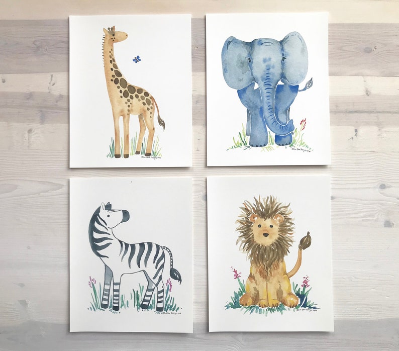 Pu&ograve; includere: Quattro illustrazioni ad acquerello di animali su carta bianca. Le illustrazioni sono di una giraffa, un elefante, una zebra e un leone. La giraffa &egrave; marrone con un motivo a macchie marrone chiaro. L'elefante &egrave; blu. La zebra &egrave; bianco e nero. Il leone &egrave; marrone con una criniera marrone chiaro.