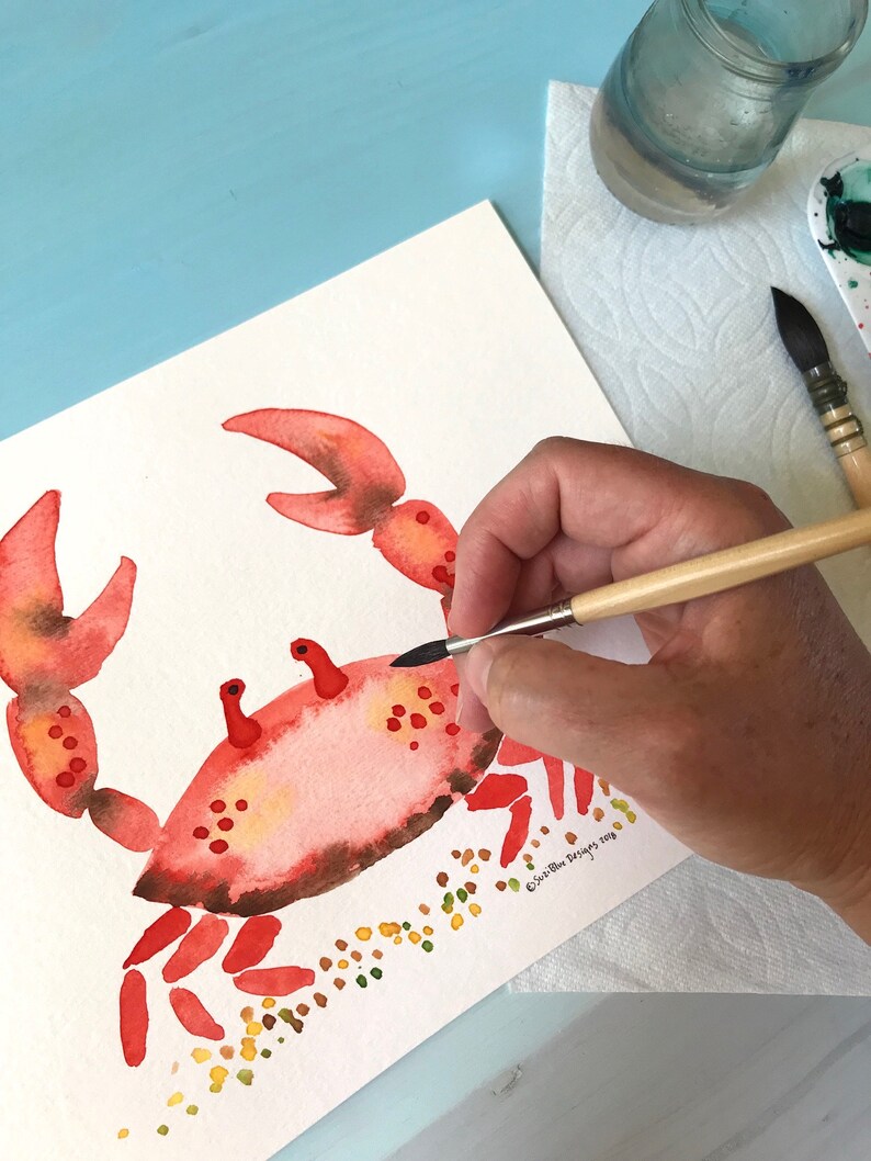 May include: A watercolor painting of a red crab with brown accents on a white background. The crab is surrounded by small yellow and green dots. The artist's signature is in the bottom right corner.