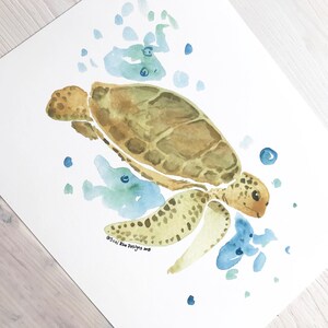 May include: Watercolour painting of a sea turtle swimming in blue water with green and blue watercolour splatter. The turtle is brown and green with a yellow underside. The painting is signed "@Suzi Blue Designs 2018".