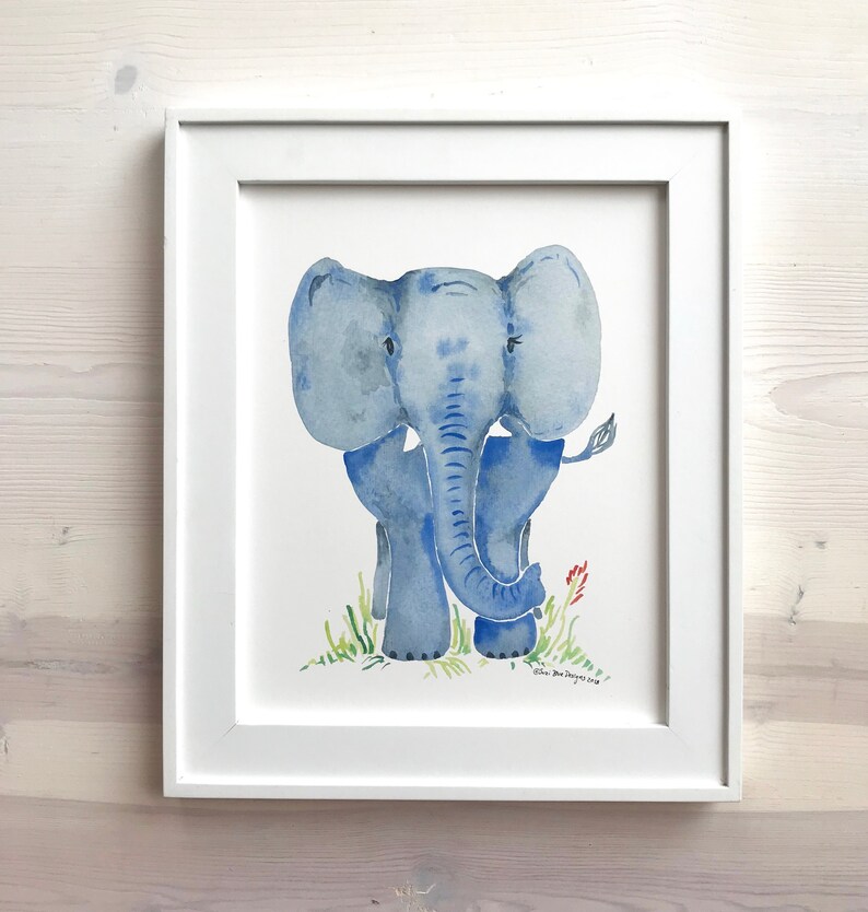 Pu&ograve; includere: Un dipinto ad acquerello di un elefante blu in piedi su un prato verde. L'elefante ha una lunga proboscide e grandi orecchie. Il dipinto &egrave; incorniciato in una cornice bianca.
