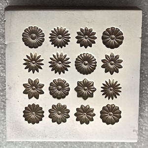 Könnte beinhalten: Eine quadratische weiße Silikonform mit einem Raster aus sechzehn vertieften Blumenmotiven. Die Form enthält vier Reihen und vier Spalten mit verschiedenen Blumenformen, jede mit ausgeprägten Blütenblattmustern, zum Gießen oder Basteln.