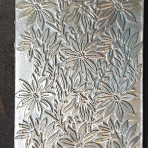 以下が含まれることがあります： 銀色のエンボス加工が施された革で、花柄が施されています。デザインは、花と葉の繰り返しパターンになっています。