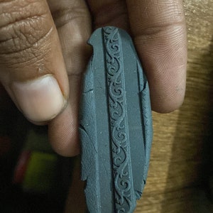 Könnte beinhalten: Ein dunkelgraues, strukturiertes, rechteckiges Objekt mit einem dekorativen Design am Rand. Das Objekt ist an einer Seite leicht abgebrochen.