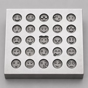 Puede incluir: Un bloque metálico cuadrado de tono plateado que presenta una cuadrícula de veinticinco hendiduras circulares. Cada hendidura contiene una cara emoji grabada distinta, incluyendo expresiones como sonreír, reír, guiñar, besar y otras.