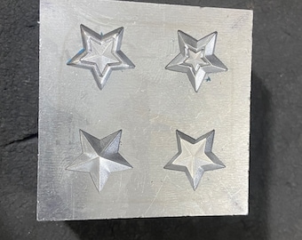 May include: A metal mold with four star-shaped impressions. The mold is made of a light gray metal and has a smooth surface.