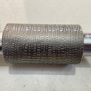 May include: A silver metal roller with a textured surface. The roller has a smooth, cylindrical handle on each end.