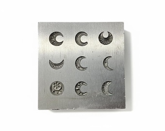 May include: A square, silver metal stamp block with nine different crescent moon designs. The moons vary in style, with some featuring detailed patterns and others being simple curves. The block is set against a white background.