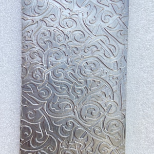 May include: A silver metal sheet with an intricate, embossed pattern of swirling, floral designs.