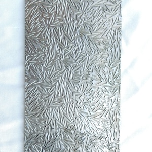 Könnte beinhalten: Eine silberne Metallplatte mit einem strukturierten Muster aus kleinen, scharfen geometrischen Formen. Die Platte ist rechteckig und hat eine glatte, polierte Oberfläche.