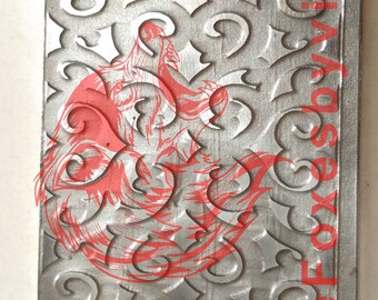 May include: A silver metal sheet with a decorative embossed pattern. The pattern is a repeating design of swirls and curves. The sheet has a slightly textured surface. The text "Five Foxes" is printed on the right side of the sheet.