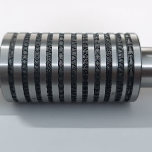 Könnte beinhalten: Eine silberne Metallrolle mit einer Reihe verschiedener Muster, die in die Oberfläche graviert sind. Die Rolle hat an beiden Enden eine glatte, zylindrische Welle.