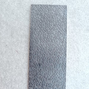May include: A black textured sheet of paper with a floral pattern embossed on the surface.