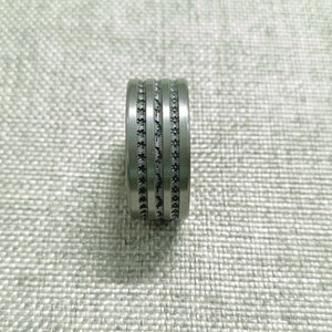 May include: A silver ring with two black bands around the center.
