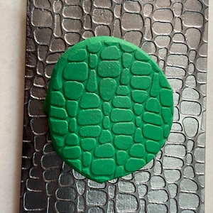 Op de afbeelding: Een ronde groene siliconen mal met een getextureerd oppervlak dat lijkt op een geplaveid pad.