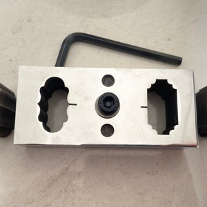 Puede incluir: Un juego de herramientas de metal para hacer joyas con un bloque central con varios recortes con forma, acompañado de dos piezas de metal a juego y una llave hexagonal negra. El juego está diseñado para dar forma al metal.