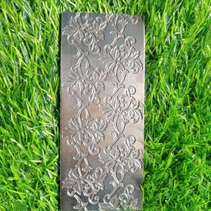 May include: A silver metal sheet with an embossed floral pattern. The pattern is intricate and detailed, with a repeating design of flowers and leaves.