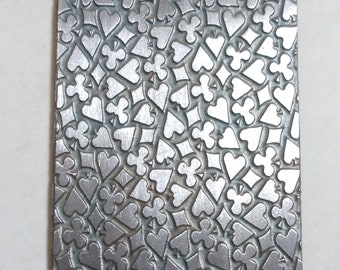 May include: A silver metal sheet with a repeating pattern of embossed hearts, clubs, diamonds, and spades.