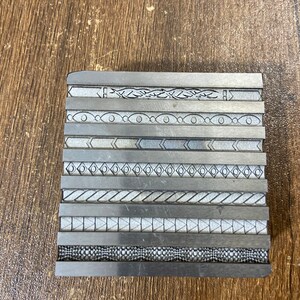 May include: A metal block with a series of different engraved patterns, including geometric shapes, lines, and swirls.