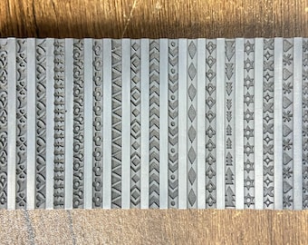 May include: A set of 20 metal stamps with different decorative border designs. The stamps are arranged in a row on a wooden surface.