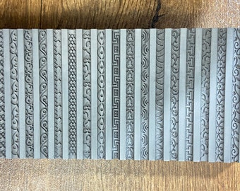 May include: A set of 24 metal stamps with different decorative border designs. The stamps are arranged in a row on a wooden surface.