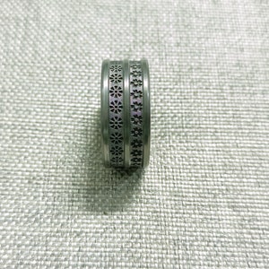 May include: A silver ring with a patterned design. The ring has a double band with a repeating pattern of small flowers.