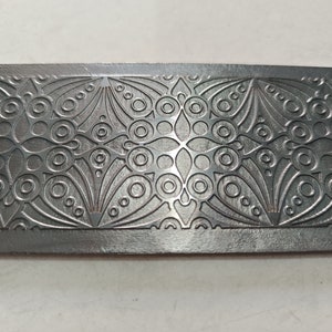 Puede incluir: Una placa de metal plateado con un diseño en relieve intrincado de círculos repetidos y motivos florales.