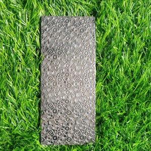 May include: A silver metal sheet with a textured pattern of circles and ovals. The sheet is lying on a bed of green artificial grass.