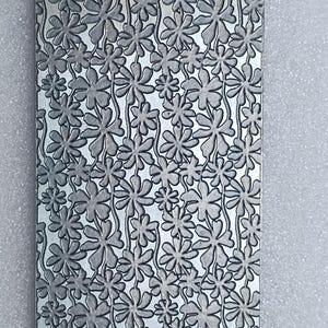 May include: A silver metal sheet with a repeating embossed pattern of small flowers. The flowers are arranged in rows and have a slightly raised texture.