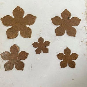 May include: Five different sized, copper-colored metal flower shapes on a white background.