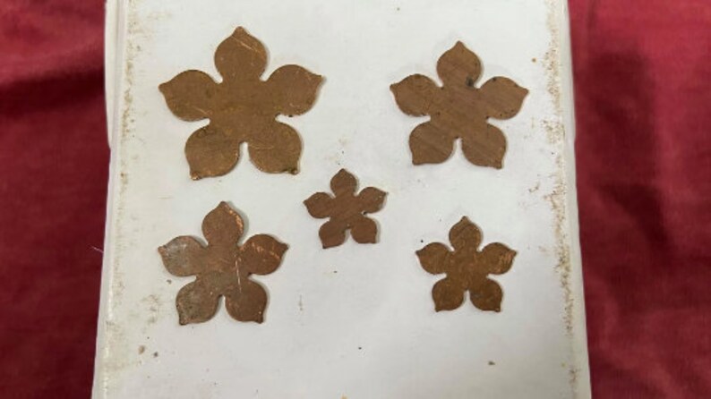 May include: Five different sized, copper-colored metal flower shapes on a white background.