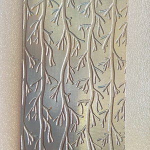 May include: A silver metal plate with a raised design of branches and leaves. The design is embossed and has a subtle sheen.