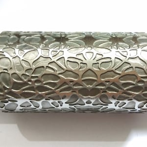 以下が含まれることがあります： 複雑な花の模様が刻まれた銀色の金属製のローラー。ローラーは滑らかで磨かれた表面を持っており、クラフトや装飾に使用するために設計されています。