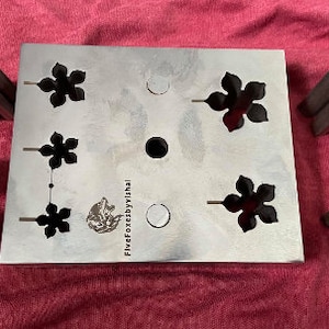 May include: A metal plate with five different sized flower-shaped cutouts. The plate is surrounded by six metal punches with flower-shaped ends. The plate is labeled "FiveFoxesbyVishal".