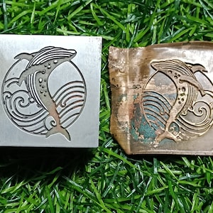May include: A metal stamp with a whale jumping out of the water design. The stamp is used to create an impression on a surface. The design is also shown on a piece of metal that has been stamped.
