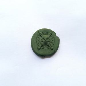 May include: A dark green round wax seal with a raised design of a skull and cross swords inside a circle.