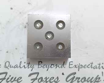 May include: A metal stamp with five different designs, including a heart, a star, a diamond, and two other geometric shapes. The stamp is silver in color and has a square shape.