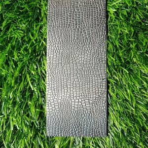 May include: A close-up of a gray textured rectangular piece of material with a crocodile skin pattern.