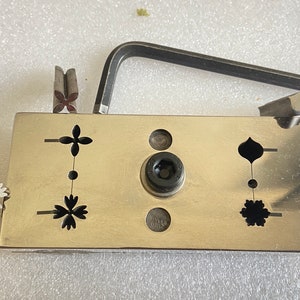 May include: A metal tool with a silver finish and a black handle. The tool has four different dies for creating shapes, including a flower, a teardrop, and a circle. The tool is used for crafting and jewelry making.