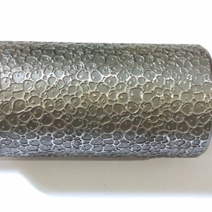 Könnte beinhalten: Eine silberne Metallrolle mit einer strukturierten Oberfläche. Die Rolle hat an beiden Enden eine glatte Welle.