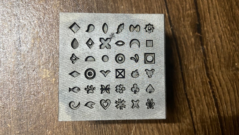 May include: A metal stamp block with 36 different designs, including hearts, stars, flowers, animals, and geometric shapes.