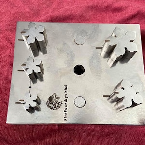 May include: A metal punch set with five different flower-shaped punches. The punches are arranged in a grid pattern on a metal plate. The plate is labeled "FiveFoxesbyVishal".