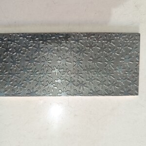 May include: A silver metal sheet with a repeating pattern of embossed, stylized starbursts.