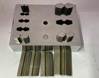 Może przedstawiać: Metalowe narzędzie z wieloma szczelinami do gięcia metalowych pasków. Narzędzie wykonane jest z polerowanego metalu i ma srebrne wykończenie. Pod narzędziem znajduje się kilka wygiętych metalowych pasków.