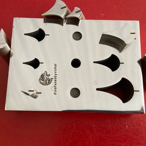 May include: A metal tool with multiple cut-out shapes, including circles and teardrop shapes. The tool is labeled "FiveFoxesbyVishal".