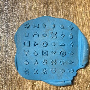 May include: Blue rubber stamp with a variety of symbols and designs, including stars, hearts, leaves, and geometric shapes.