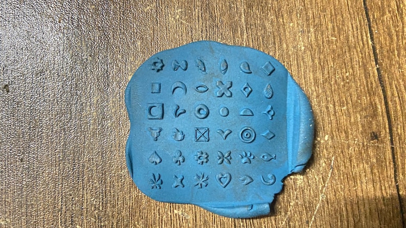May include: Blue rubber stamp with a variety of symbols and designs, including stars, hearts, leaves, and geometric shapes.