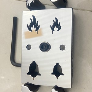 May include: A metal punch set with six different shapes, including flames and bells. The punches are arranged in a rectangular frame with a black handle.