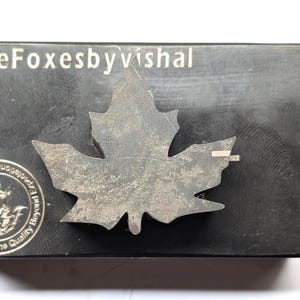 May include: A rectangular, dark gray object with a silver maple leaf emblem. The text "FiveFoxesbyVishal" is printed in white at the top. A circular logo with text is on the lower left.