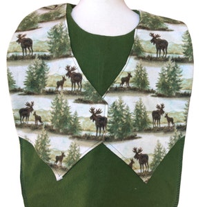 May include: A green fleece bib with a moose and pine tree pattern. The bib has a V-neck opening and is designed to protect clothing from spills and messes.